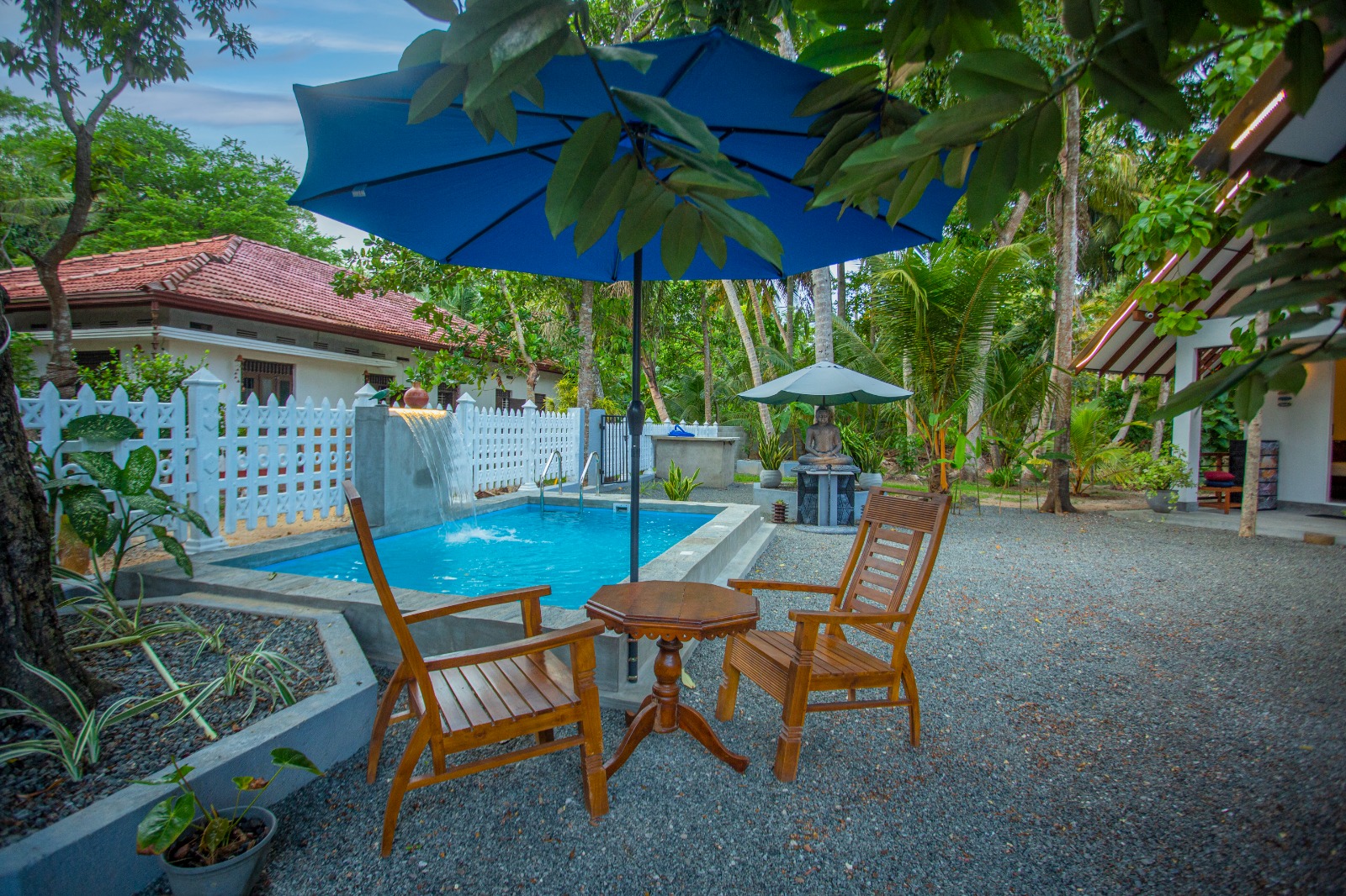 Pool with wooden chairs and blue umbrellas in a tropical garden